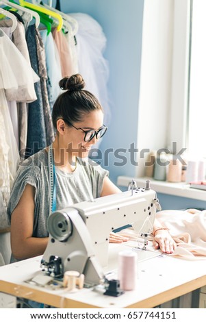 closeup portrait of young woman seamstress sitting and sews on sewing machine. Dressmaker work on the sewing machine. Tailor making a garment in her workplace. Hobby sewing as a small business concept