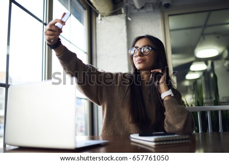 Attractive confident woman in stylish spectacles posing for smartphone while taking good picture.Gorgeous hipster girl making selfie and sharing image with friends in social network