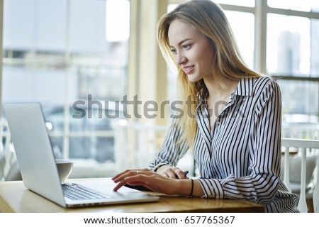 Concentrated blonde female copywriter working on creative task watching webinar for improving skills and knowledge,attractive journalist monitoring latest news on websites using laptop computer