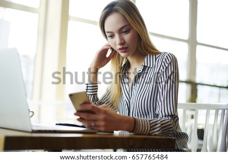 Pensive blonde female manager in formal wear checking email box waiting for feedback while working in cafe interior, concentrated young freelancer paying for receipt online receiving notification