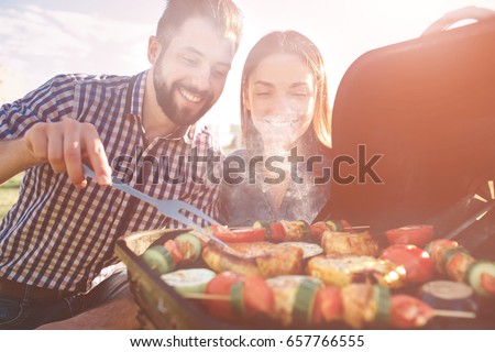 Friends making barbecue and having lunch in the nature. Couple having fun while eating and drinking at a pic-nic - Happy people at bbq party