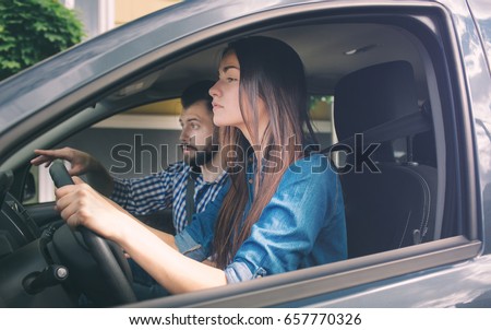 Driving test. Young serious woman driving car feeling inexperienced, looking nervous at the road traffic for information to make appropriate decisions. Man is an instructor, controlling and checking Royalty-Free Stock Photo #657770326