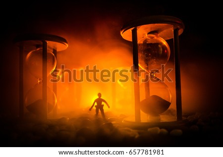 Time concept. Silhouette of a man standing between hourglasses with smoke and lights on a dark background. Surreal decorated picture