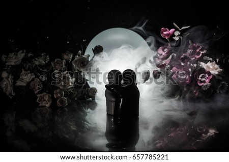 Two doll hugging on table with flowers and moon decoration Lighted background with smoke.Love concept. Greeting or gift card design idea. Silhouette of hugging couple