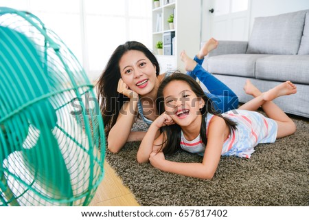 happy family of mother and daughter making same posing looking at camera enjoying electric fan cool wind in summer day with selective focus photo.