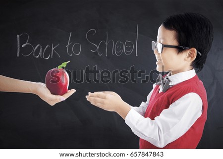 Picture of a cute little boy receiving apple fruit in the classroom with text Back to School on the blackboard