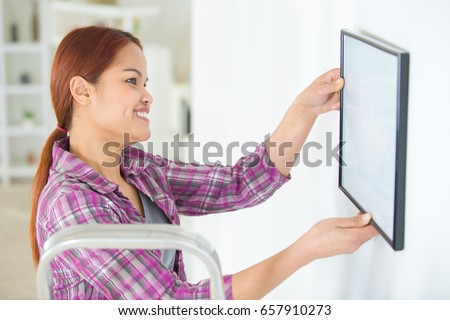 smiling asian girl hanging frame on the wall