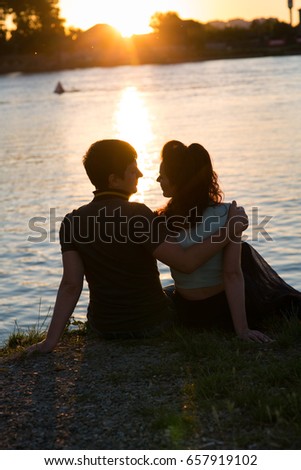 Beautiful young couple sitting on the river bank at sunset
