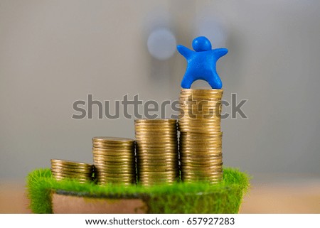 Miniature human figure made from blue plasticine with coins on wooden table. shallow focus, soft tone. business concept.