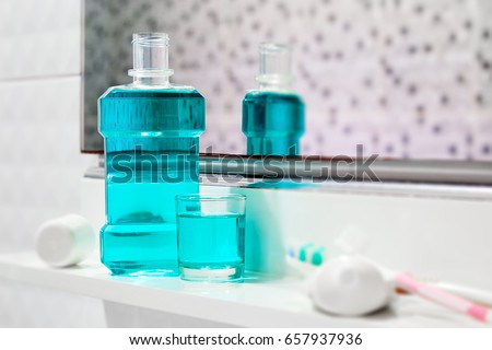 Oral cleanser for good oral health, Bottle and glass of mouthwash on bath shelf with blurred toothbrush and toothpaste in foreground Royalty-Free Stock Photo #657937936