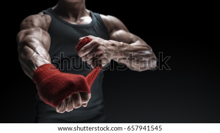 Close-up photo of strong man wrap hands on black background with copy space for text Man is wrapping hands with red boxing wraps