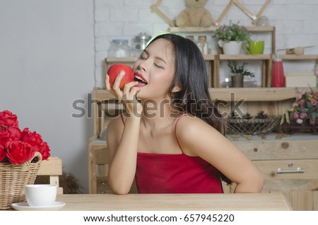 Beautiful young woman is holding an apple On the kitchen background.