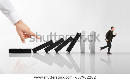 Man running from falling huge dominoes while male hand pushing them on light background. Concept of irresponsible business strategy Royalty-Free Stock Photo #657982282