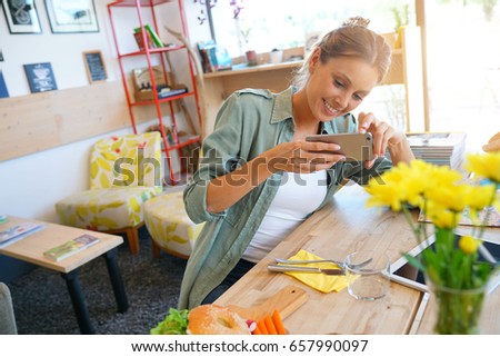 Trendy girl in restaurant taking picture of colourful dish with smartphone