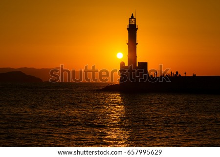 Silhouette of lighthouse in sea at sunset in the city of Chania, island of Crete, Greece. Beautiful seascape at sunset