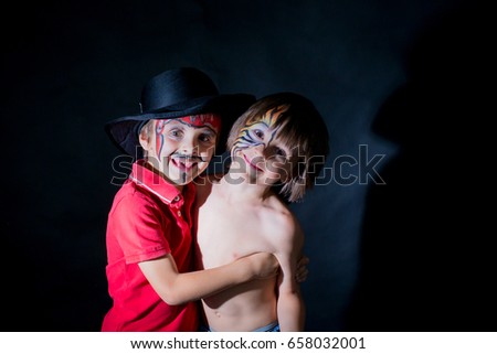 Two children, brothers, painted as tiger and pirate, playing together in studio, isolated image on black background, dramatic light,