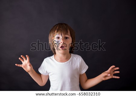 Sweet preschool child, painted as tiger, playing in studio, isolated image on black background, dramatic light