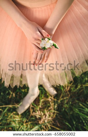 Ballerina in white tutu and pointe shoes stay in green nature and holding flower in the hands at sunset. Concept of female tenderness and harmony life