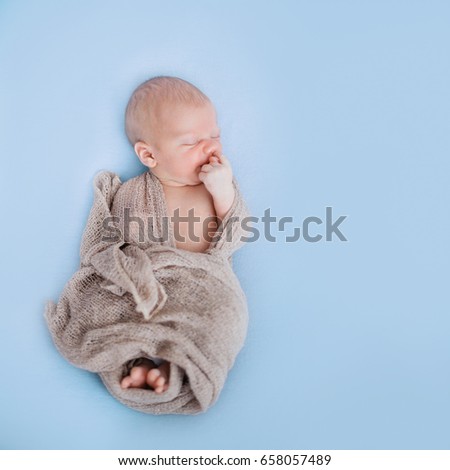Studio shoot of cute 10 days old newborn baby sleeping on a soft blue blanket in a wrap, square picture