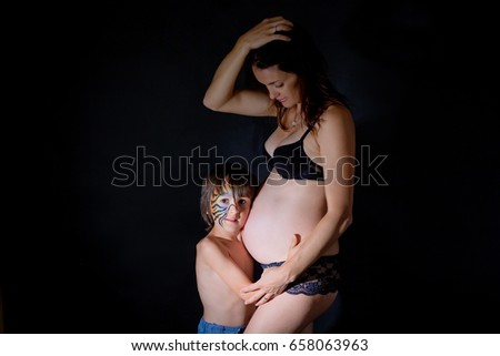 Double portrait of young pregnant woman and her child boy with painted face as tiger, isolated on black, dramatic light, studio shot, black background