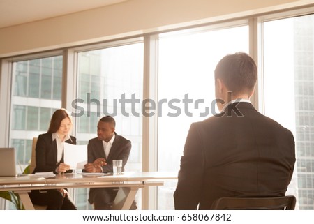Nervous applicant sitting on chair waiting for result after job interview, worried businessman awaits for approve reject decision while expert group considering claim application complaint, rear view Royalty-Free Stock Photo #658067842