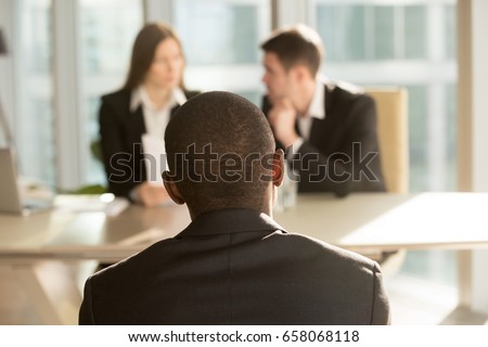 Nervous african-american applicant waiting for result after job interview, hr managers making decision at background, black businessman patiently awaits for claim complaint consideration, back view Royalty-Free Stock Photo #658068118