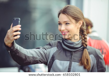 The girl takes pictures of herself on the phone, a long braid and a beautiful smile, in moto equipment