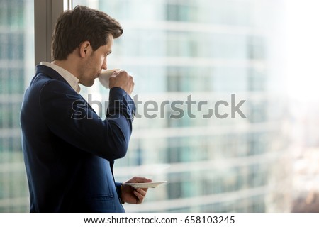 Thoughtful businessman drinking coffee, looking through window at big modern city, having break, deep in thoughts, enjoying view, waiting for meeting to start, making business decision, copy space Royalty-Free Stock Photo #658103245