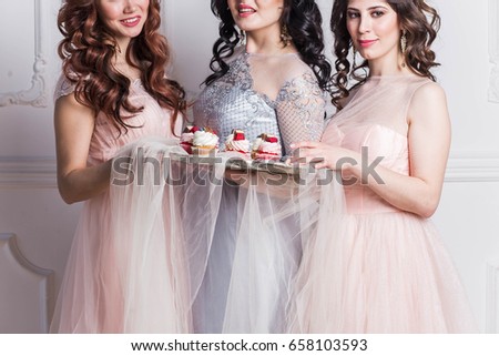 three beautiful girls in pink dresses professional makeover are smiling, happy, laughing with a tray of delicious cupcakes, bachelorette party, emotions on a white background in Studio
