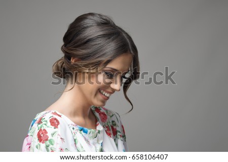 Portrait of shy timid smiling beautiful woman looking down expression over gray studio background. Royalty-Free Stock Photo #658106407