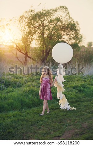 Little beautiful girl with big balloon near the lake at sunset