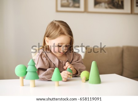 Little beautiful girl playing with green wooden trees . Child playing with educational toys at kindergarten or in the room. 