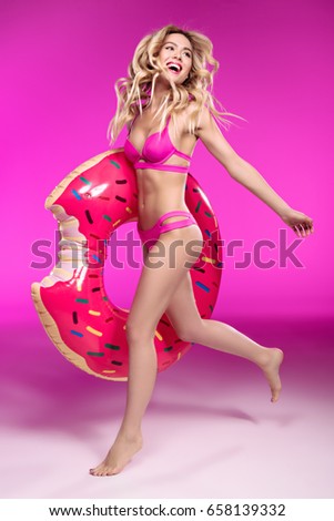 Happy young woman in swimsuit running with swimming tube in shape of doughnut