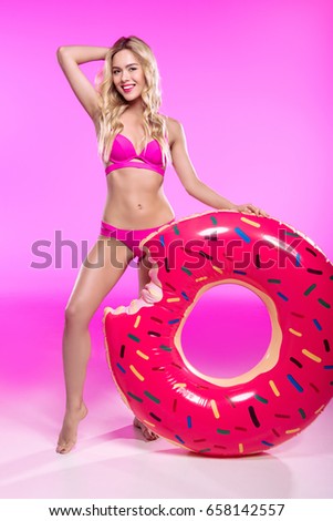 Smiling young woman in swimsuit posing with swimming tube in shape of doughnut