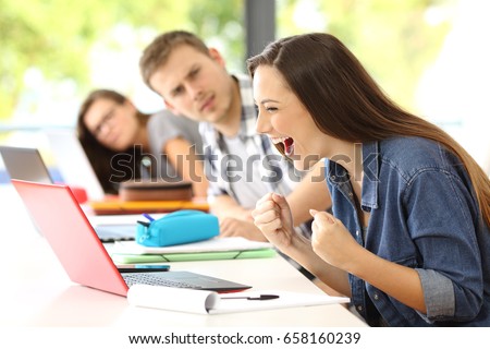 Excited student receiving good news on line in a classroom with her surprised classmates looking