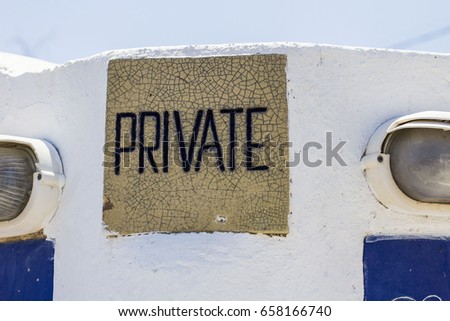 Decorative tile with word "Private" written on it inserted into the white wall. Photo made at Santorini, Greece