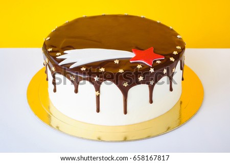 A birthday cake poured with chocolate, decorated with confectionery sprinkling stars and a comet image on a yellow and white background. Picture for a menu or a confectionery catalog.