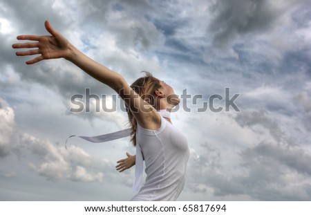 Young woman with white ribbon and raised hands on clouds background