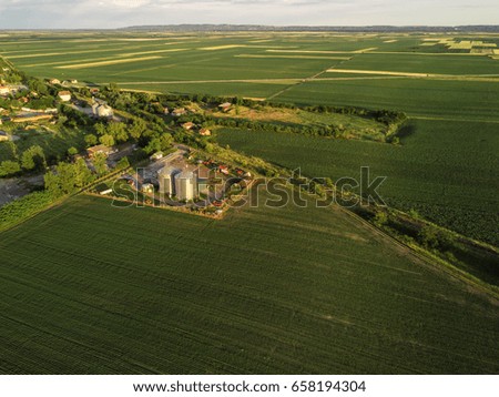 Aerial view of countryside landscape from drone pov - cultivated fields, silos and village in the distance