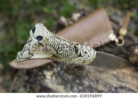 A beautiful handle close up of a handmade knife, In the shape of a wolf's head. Handmade, elk horn, damask steel. Against the background of the tree bark.