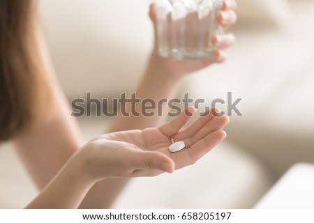 Close up photo of one round white pill in young female hand. Woman takes medicines with glass of water. Daily norm of vitamins, effective drugs, modern pharmacy for body and mental health concept Royalty-Free Stock Photo #658205197