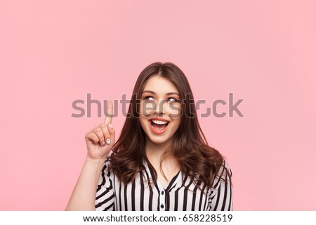 Young pretty girl holding finger up having idea and posing on pink background.  Royalty-Free Stock Photo #658228519