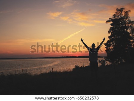 Beautiful summer scene. Photo showing the silhouette of a person showing joy by the sunset.