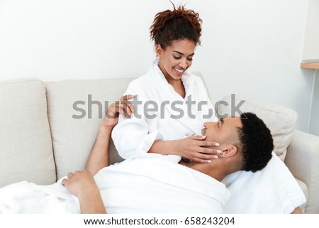 Image of young happy african loving couple sitting indoors at home and looking aside.