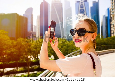 Blonde lady looks over her shoulder while she takes picture of beautiful skyscrapers in Dubai