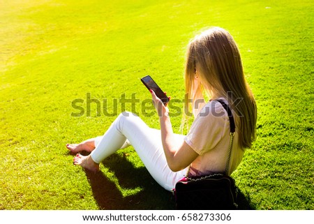 Elegant lady checks her iPhone sitting on green lawn in park