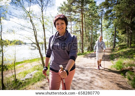 Summer sport in Finland - nordic walking. Man and mature woman hiking in green sunny forest. Active people outdoors. Scenic peaceful Finnish summer landscape. Royalty-Free Stock Photo #658280770