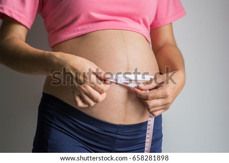 Pregnant woman measuring her belly with tape measure.
