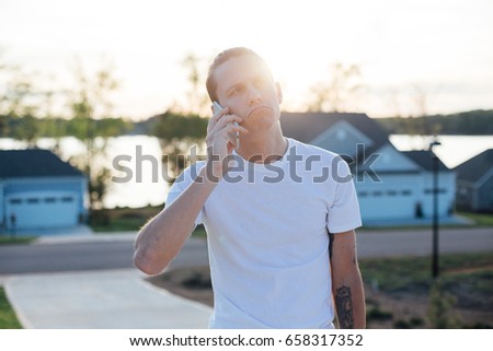 Attractive funny cute looking male teenager from millennial generation makes not bad meme face while talking on phone with his parents or friends