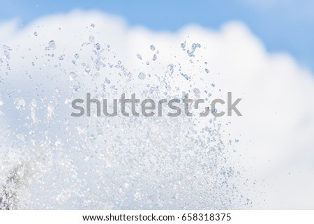 Water drops from the ocean waves in the air on the sky and clouds background - close up texture photo.